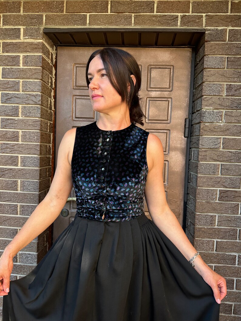 May include: A black sleeveless top with a paisley pattern and a black skirt. The top has a button closure and a belt.