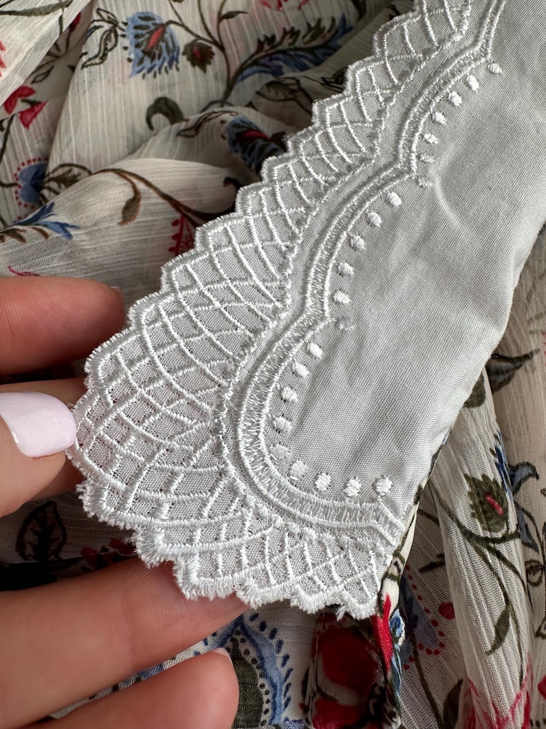 May include: White lace trim with a scalloped edge. The lace has a delicate floral pattern.
