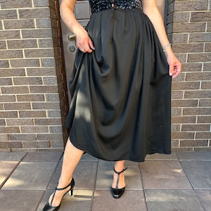 May include: A black skirt with a gathered waistline and a flowing silhouette. The skirt is paired with a black top with a floral print and black heels.