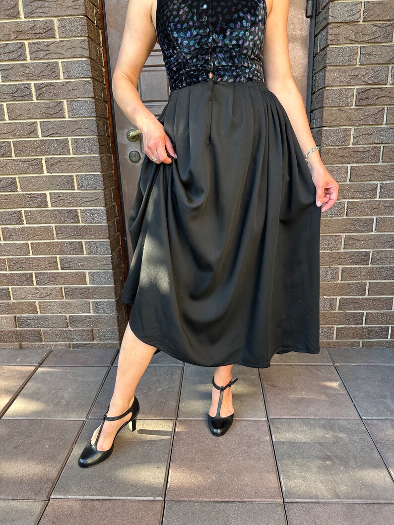 May include: A black skirt with a gathered waistline and a flowing silhouette. The skirt is paired with a black top with a floral print and black heels.