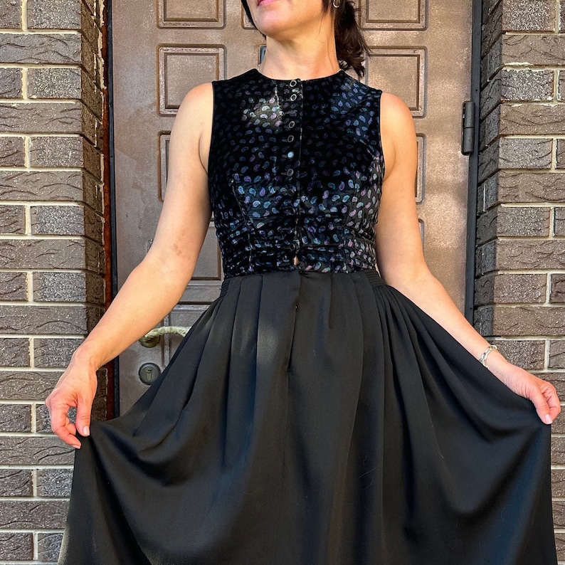 May include: A black velvet top with a button-up front and a scattered pattern of small purple and blue shapes. The top is paired with a black skirt that has a gathered, flowing silhouette.