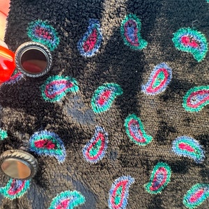 May include: Black velvet fabric with a paisley pattern in shades of blue, green, and red. The fabric has three black buttons with silver accents.