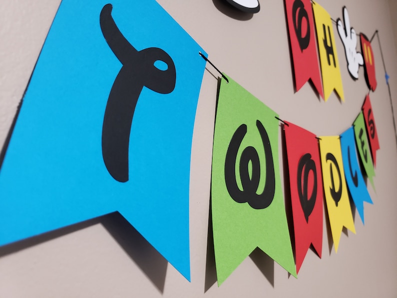 May include: A vibrant banner spelling "TWOODLES" in black on blue, green, red, and yellow pennants. The banner also features a Mickey Mouse cutout and the words "OH BOY".