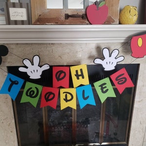 May include: A vibrant banner spelling "TWOODLES" in black letters on individual flags. The banner is decorated with Mickey Mouse-themed cutouts, including a black silhouette of Mickey's head, white gloves, and red shorts.