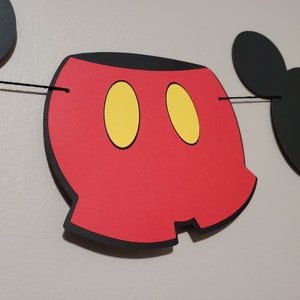 Puede incluir: Bandera roja y negra con tem&aacute;tica de Mickey Mouse con orejas negras y c&iacute;rculos amarillos. La bandera est&aacute; enhebrada con una cuerda negra.