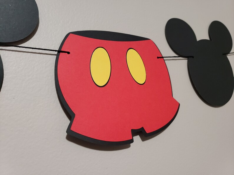 Puede incluir: Bandera roja y negra con tem&aacute;tica de Mickey Mouse con orejas negras y c&iacute;rculos amarillos. La bandera est&aacute; enhebrada con una cuerda negra.