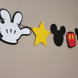 Puede incluir: Una pancarta de fiesta con tem&aacute;tica de Mickey Mouse con guantes de Mickey Mouse blanco y negro, estrellas amarillas, orejas de Mickey Mouse negras y pantalones cortos de Mickey Mouse rojos.