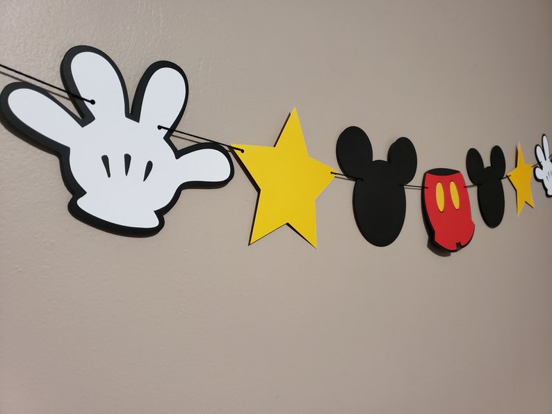 Puede incluir: Una pancarta de fiesta con tem&aacute;tica de Mickey Mouse con guantes de Mickey Mouse blanco y negro, estrellas amarillas, orejas de Mickey Mouse negras y pantalones cortos de Mickey Mouse rojos.