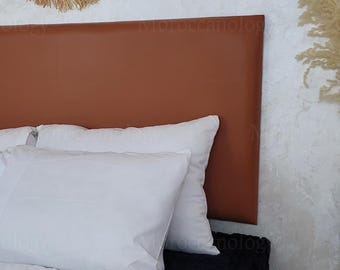 Könnte beinhalten: Ein braunes Leder-Kopfteil mit weißen Kissen und Bettwäsche. Das Kopfteil ist rechteckig und hat eine glatte Oberfläche. Die Kissen sind flauschig und die Bettwäsche ist weiß. Das Wort "Moroccanology" ist auf dem Kopfteil aufgedruckt.