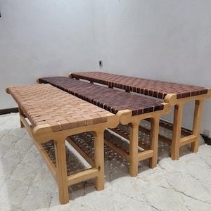 Peut inclure: Trois bancs en bois avec des assises en cuir tress&eacute;. Les bancs ont des cadres en bois brun clair et les assises sont en cuir tress&eacute; dans des tons de beige et de marron. Les bancs sont sur un tapis blanc.