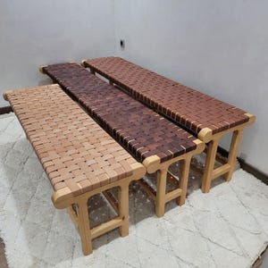 Peut inclure: Trois bancs en bois avec des assises en cuir tress&eacute; de diff&eacute;rentes nuances de marron. Les bancs ont des pieds en bois clair et un design incurv&eacute; aux extr&eacute;mit&eacute;s. Les assises sont faites de lani&egrave;res de cuir entrelac&eacute;es.