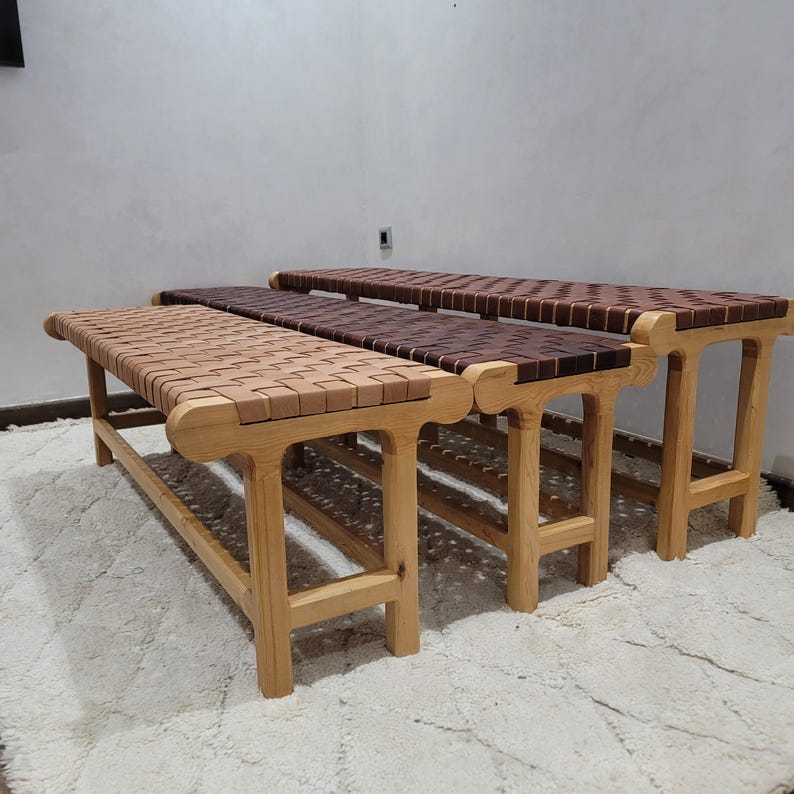 Peut inclure: Quatre bancs en bois avec des assises en cuir tress&eacute;. Les bancs ont une finition en bois naturel et sont dispos&eacute;s en rang&eacute;e. Les assises en cuir varient en couleur, allant du beige clair au marron fonc&eacute;. Les bancs sont sur un tapis blanc.
