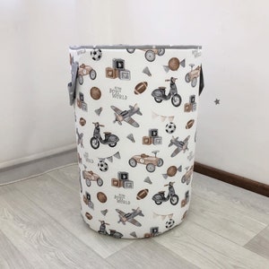 May include: A cylindrical storage basket with a white background and a repeating pattern of vintage vehicles, sports balls, and building blocks. The text "Retro Boys World" is printed on the side. The basket has gray handles and trim.