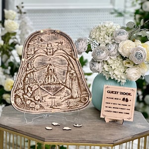 Könnte beinhalten: Ein hölzernes Gästebuch in Form von Darth Vaders Helm mit einem Star Wars-Design. Das Schild lautet "Gästebuch, Bitte unterschreiben Sie ein & legen Sie es in den Rahmen, wir werden unsere Lieben, die gekommen sind, nie vergessen."