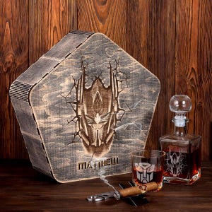 May include: A wooden box with a laser-engraved image of a robot face. The box is labeled "MATTHEW". The box is next to a glass decanter and two glasses, all with the same robot face design. A cigar and a cigar cutter are also included.