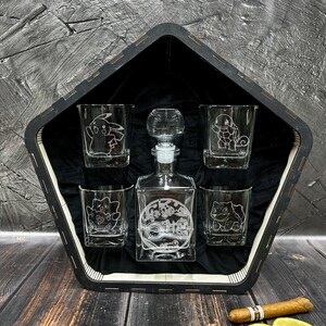 May include: A wooden box with a pentagon shape holds a set of five clear glass decanters. The decanters are etched with images of Pokemon characters. The box is lined with black velvet.