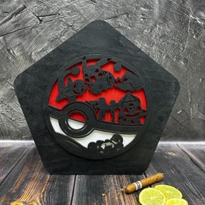 May include: Black wooden plaque with a red and white Pokeball design. The Pokeball features a silhouette of multiple Pokemon characters.