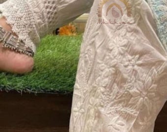Può includere: Pantaloni bianchi ricamati con motivi floreali e finiture in pizzo. I pantaloni presentano un dettaglio con polsino abbottonato e sono realizzati in un tessuto leggero. Il design include ricami intricati e un'estetica delicata e femminile.