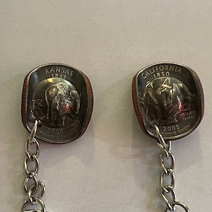 May include: Two silver keychains with quarter-sized coins attached. The coins are from the United States Mint's America the Beautiful Quarters Program. The left coin features a bison and the text "Kansas 1861". The right coin features a Yosemite Valley scene and the text "California 1850". Both coins have the year "2005" on them.