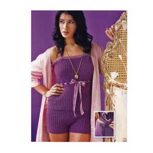 May include: A purple knitted sleepwear set with a satin ribbon detail. The top is sleeveless and the shorts are short. The model is wearing a pink robe.