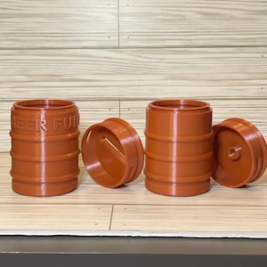 May include: Three brown plastic beer keg piggy banks with a slot on the top. One keg has the words "BEER FUND" printed on the side.