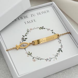 Könnte beinhalten: Ein goldfarbenes Armband mit einem Fischsymbol und einem rechteckigen Namensschild mit der Gravur "Ramona" wird in einer weißen Geschenkbox präsentiert. Die Box enthält eine Karte mit Text und einem floralen Kranzdesign.