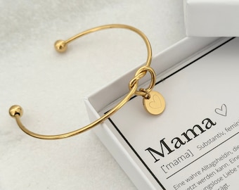May include: A gold bangle bracelet with a heart charm and a knot design. The bracelet is in a white box with a card that reads "Mama ['mama] Noun, feminine A true everyday heroine, who replaces everyone, but cannot be replaced. A woman who gives her children unconditional love and carries them in her heart for a lifetime. Synonyms: Favourite person, Superwoman, Encourager"
