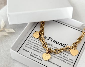 May include: A gold chain necklace with a heart charm that says "Best Friend" and another charm with two hands clasped together. The necklace is in a white box with a definition of the word "Best Friend" in German.