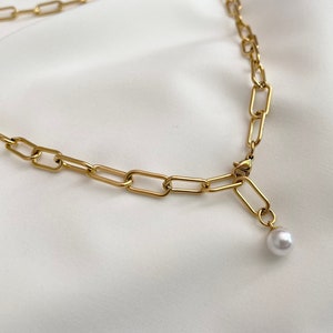 Puede incluir: Un collar de cadena dorada con un colgante de perla blanca.