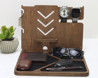 May include: A wooden organizer with compartments for a watch, phone, keys, sunglasses, and wallet. The organizer has a brown wood finish and white arrow designs.