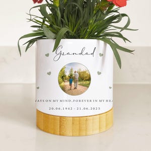 May include: A white ceramic plant pot with a bamboo base, filled with red flowers. The pot is inscribed with "Grandad" and a photo of a man and child. Text reads "ALWAYS ON MY MIND, FOREVER IN MY HEART" and dates.