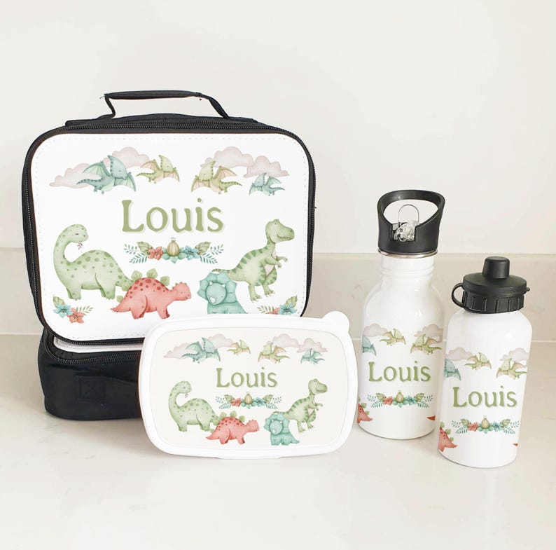 Puede incluir: Un juego de bolsa de almuerzo personalizado con tem&aacute;tica de dinosaurios. El juego incluye una bolsa de almuerzo aislada negra con una cremallera blanca, una fiambrera blanca con un dise&ntilde;o de dinosaurio verde, una botella de agua blanca con una tapa negra y una botella de agua blanca m&aacute;s peque&ntilde;a con una tapa negra. Todos los art&iacute;culos tienen el nombre "Louis" impreso en ellos.
