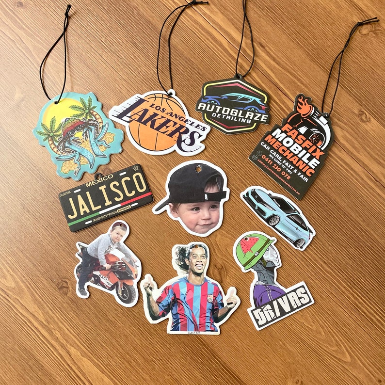 May include: Assortment of car air fresheners with various designs, including a basketball team logo, a car detailing company logo, a mobile mechanic logo, a cartoon crab, a state of Jalisco license plate, a child's face, a soccer player, and a cartoon character with a watermelon on its head.