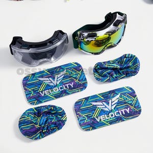 May include: Two pairs of ski goggles with clear and mirrored lenses, and four matching goggle covers. The goggles have black frames and straps. The covers and one pair of goggles have the word "VELOCITY" printed on them.