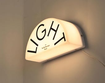 May include: A white, semi-circular wall light fixture with the word "LIGHT" in black lettering. The text "Vanilla Mountain house" is below the word "LIGHT". The fixture is mounted on a light gray wall.
