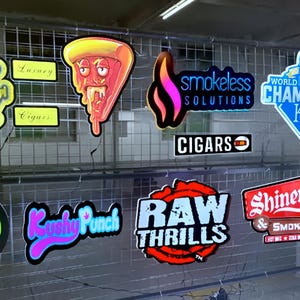 May include: A collection of colorful, illuminated signs, including a pizza slice with a face, a flame design with the text "smokeless SOLUTIONS", and signs that say "RAW THRILLS" and "CIGARS". The signs are displayed on a wire grid.