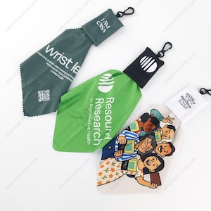 May include: Three watch lens cleaning cloths with pouches and carabiner clips. One is dark green with "wrist le" text. Another is green with "Resound Research" text. The third is white with a cartoon image.
