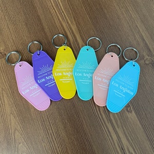 May include: Six colorful keychains with a retro motel key design. Each keychain features a white sun graphic and the text "Welcome to Sunny Los Angeles, California".
