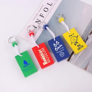 Puede incluir: Cuatro llaveros rectangulares en verde, rojo, azul y amarillo. Cada llavero tiene un cordón blanco y un anillo de metal. Los llaveros presentan texto y gráficos, incluyendo "Northwest Regional Water District", "HUMBOLDT MUSEUM", "Co Co Cabaña" y "I'm a BIG SOFTIE."