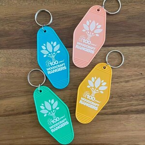May include: Four keychains in different colors, pink, yellow, blue, and green, with a white tree design and the text "100 years! Woodcraft Rangers".