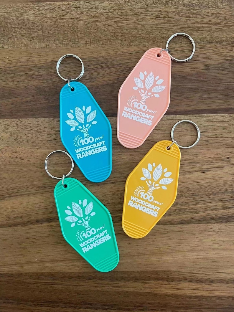 May include: Four keychains in different colors, pink, yellow, blue, and green, with a white tree design and the text "100 years! Woodcraft Rangers".