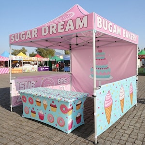 May include: A pink and white pop-up gazebo with the text "SUGAR DREAM" and "BUGAM BAKERY". The table has a blue cover with donuts, cupcakes, and ice cream cones. A large cake graphic is on the side. Other market stalls are visible.