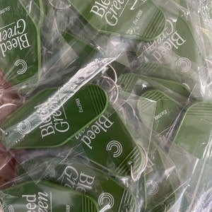 May include: A pile of green keychains with the text "Bleed Green" and "Est. 1988" on them. The keychains are in plastic packaging.