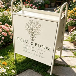 Puede incluir: Un expositor de metal color crema con un panel frontal rectangular que presenta una ilustraci&oacute;n floral de l&iacute;neas y el texto PETAL & BLOOM, FLOWERS &bull; PLANTS &bull; JOY, y Fresh Flowers, Made with Love con un peque&ntilde;o s&iacute;mbolo de coraz&oacute;n.