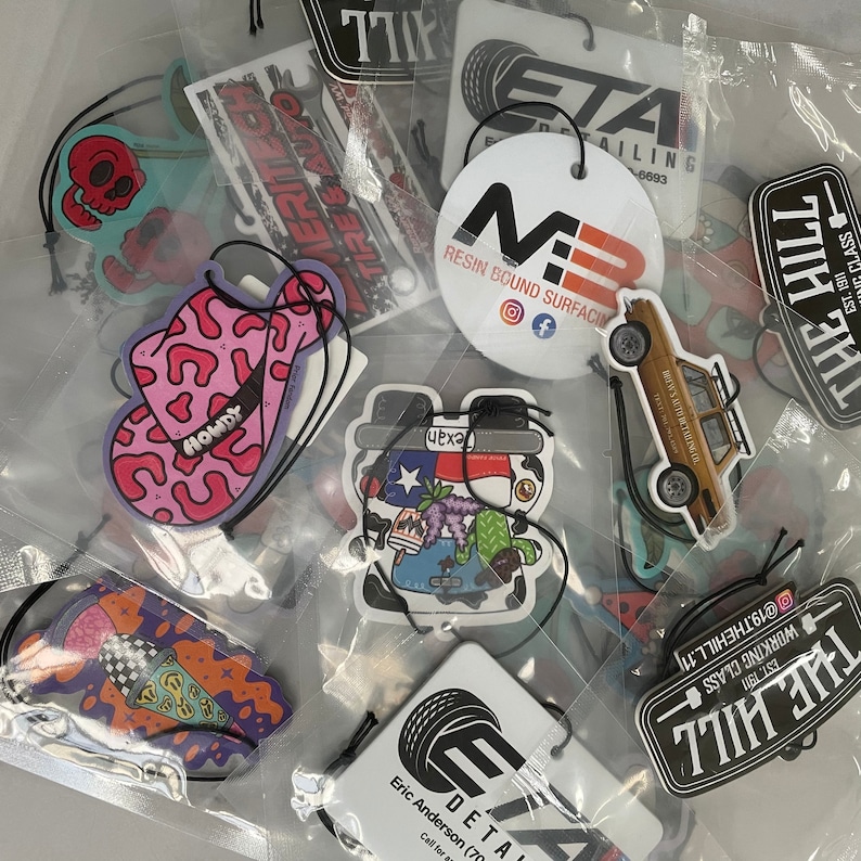 May include: Assortment of colorful car air fresheners with various designs, including a cowboy hat, a cartoon character, and a car. The air fresheners are made of paper and have a string for hanging.