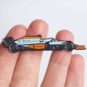 May include: A blue and orange enamel pin of a race car with the number 4 and the word "VUSE" on it.
