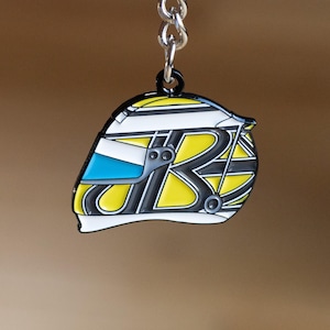 Op de afbeelding: Een gele, zwarte en witte racehelm sleutelhanger. De helm heeft een blauw vizier en een zwarte 'R' aan de zijkant.