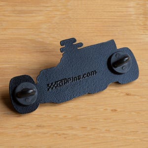 May include: Black enamel pin of a Formula 1 race car with a checkered flag design and the text "GPPINS.COM" on the back.