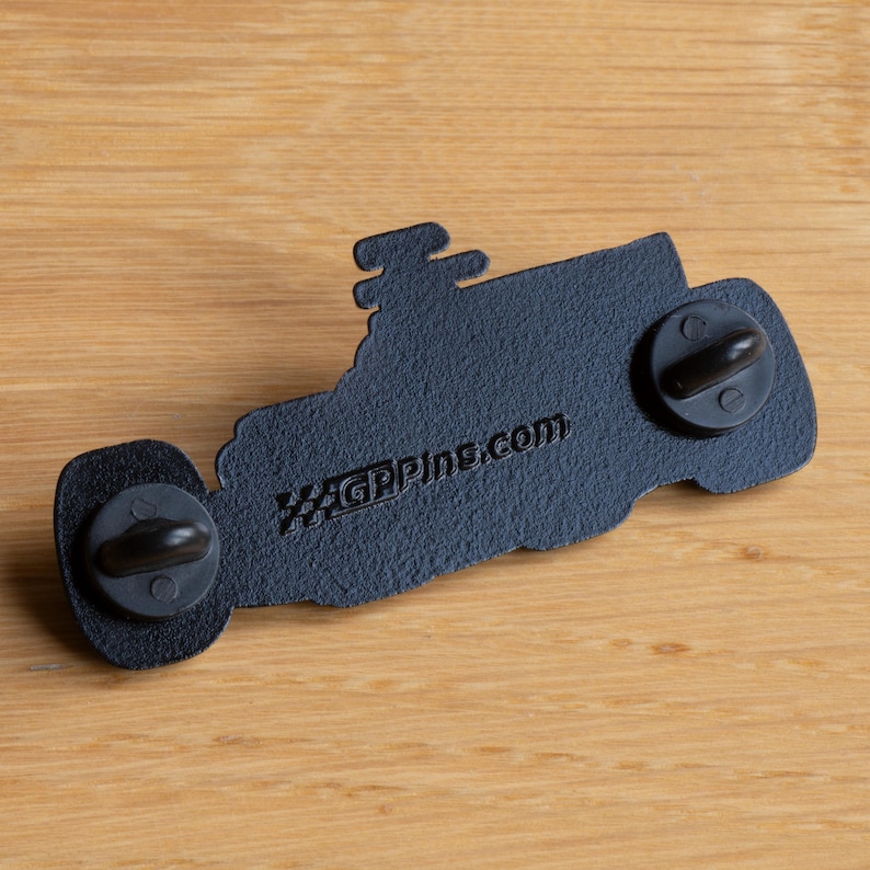 May include: Black enamel pin of a Formula 1 race car with a checkered flag design and the text "GPPINS.COM" on the back.