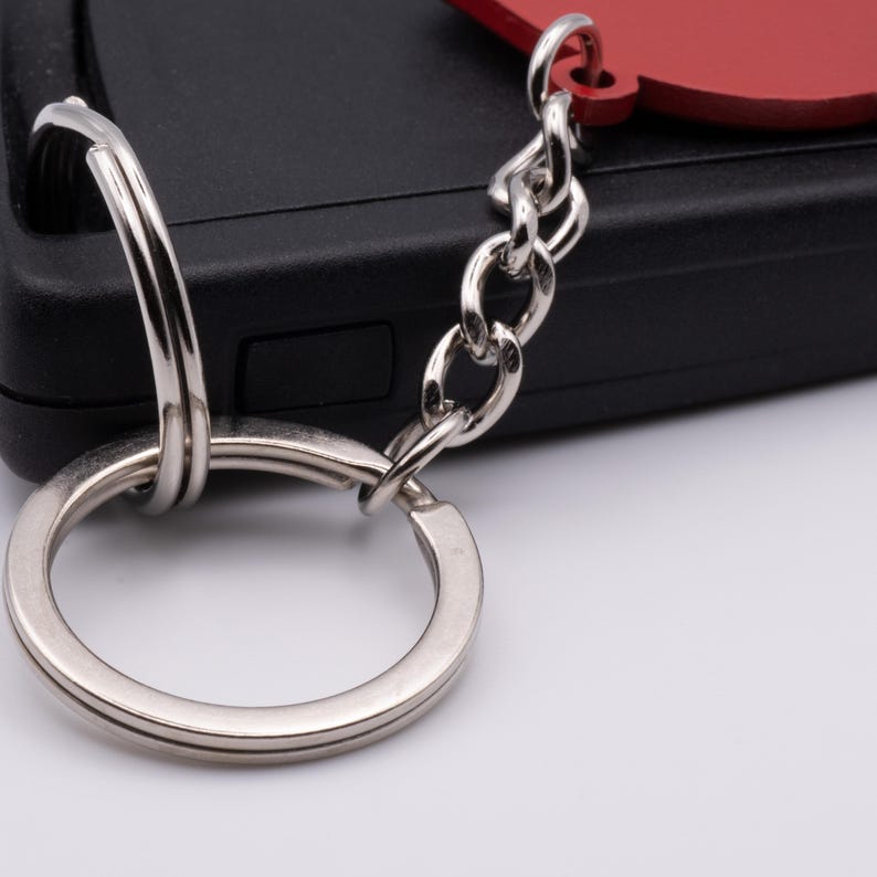 Pode incluir: Um chaveiro prateado com um charme de cora&ccedil;&atilde;o vermelho preso a um chaveiro preto.